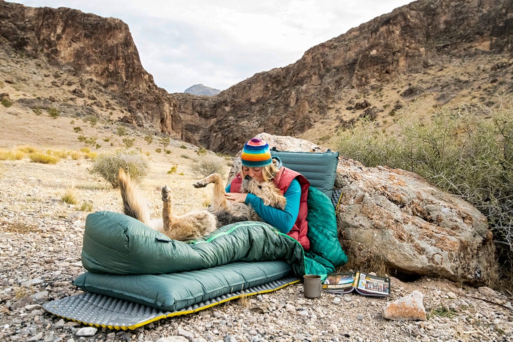 Woman cuddling with dog on sleep system in the desert