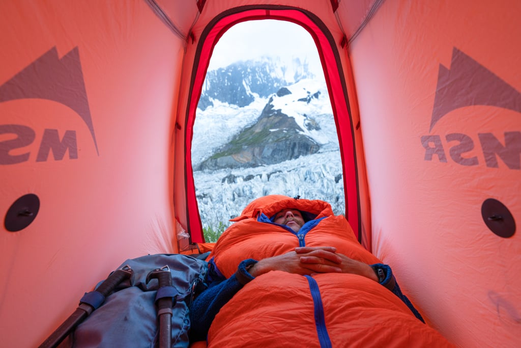 Man sleeping in sleeping bag and tent, with glaciers in background
