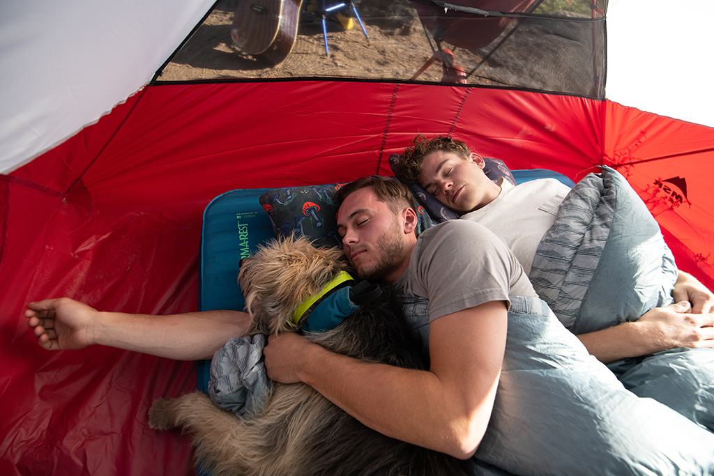 couple sleeping on thick camping mattress with camping pillows and dog