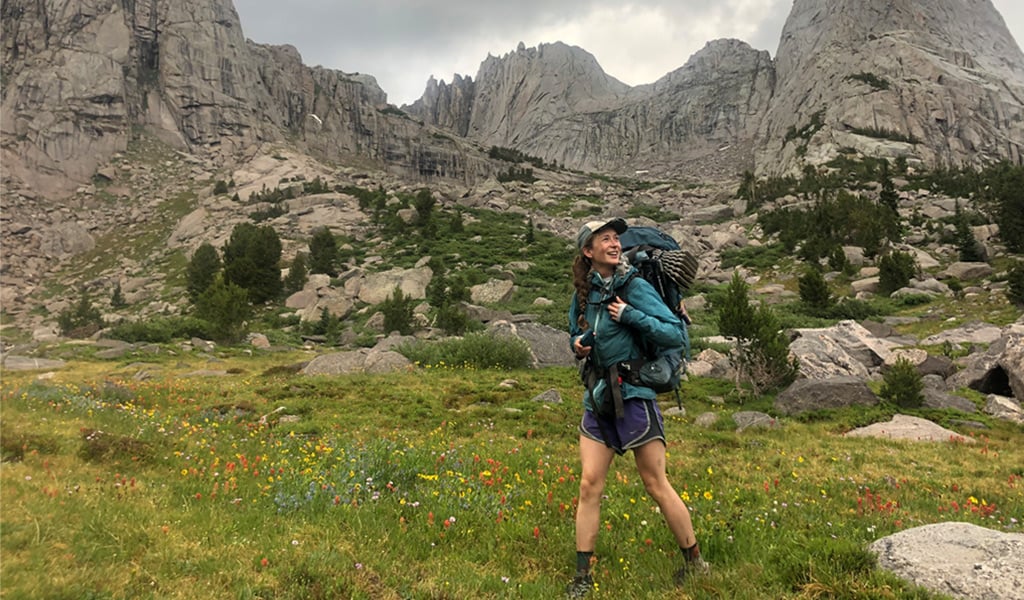 Woman hiking through meadow with mountains in background