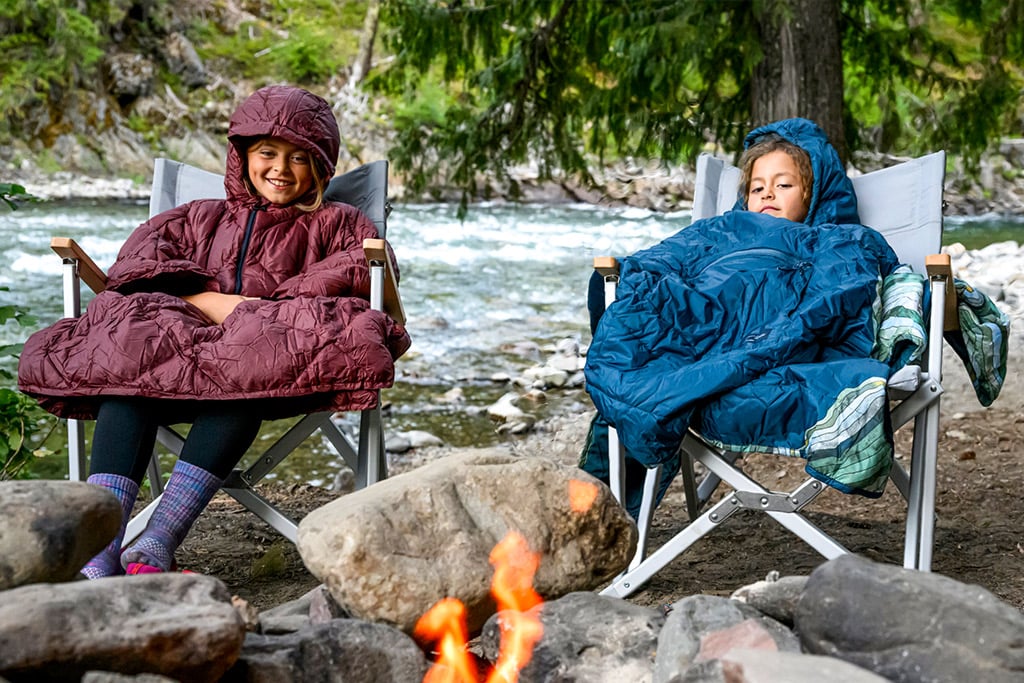 Two girls sitting by a fire in Therm-A-Rest Honcho Ponchos