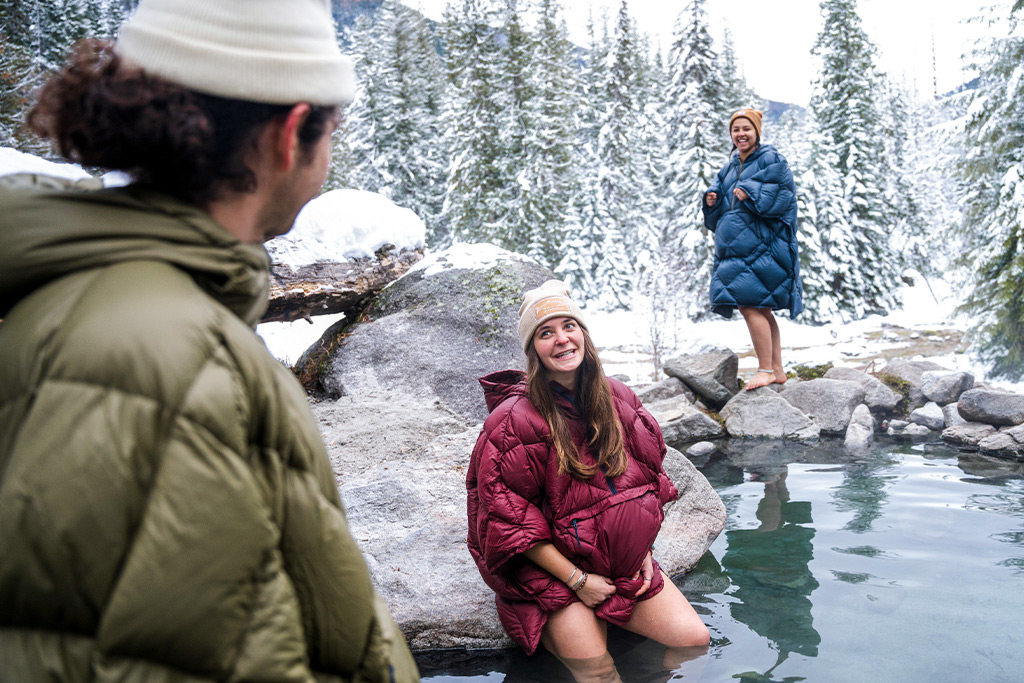 Three people in Therm-A-Rest Honcho Poncho Down taking a dip in a hot spring