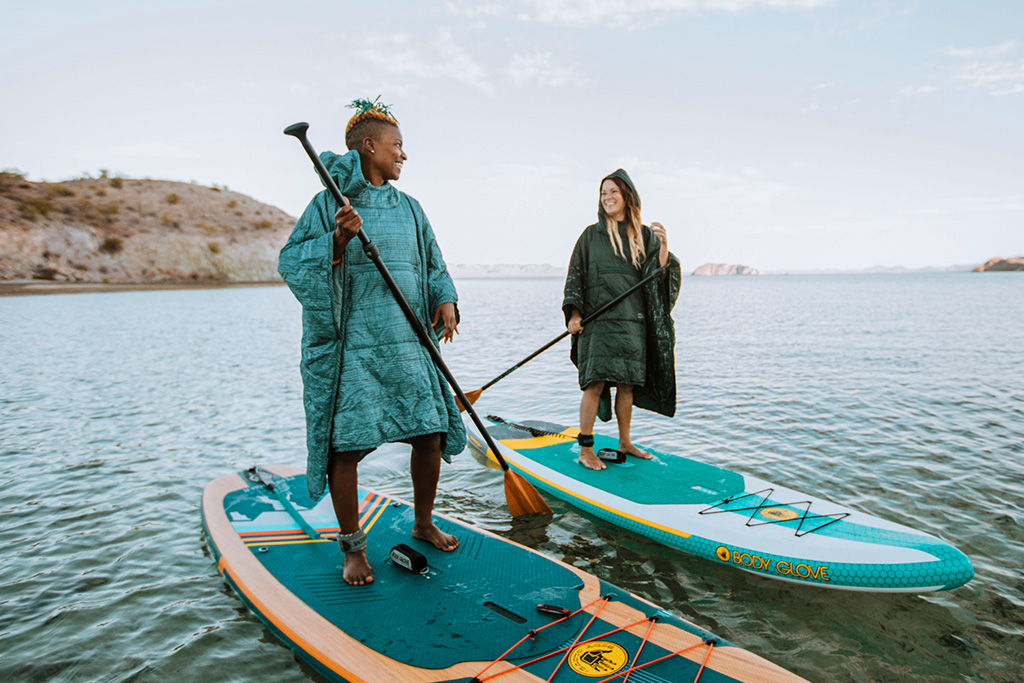 Two women paddleboarding while wearing Therm-A-Rest Honcho Ponchos