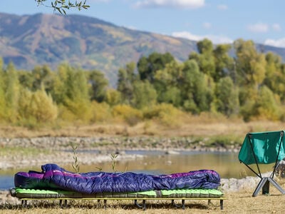 A sleeping bag, air mattress and UltraLite cot set up in front of a mountain